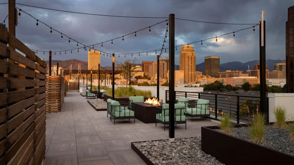 Skyhouse rooftop lounge with a fire feature, string lights, and the Salt Lake City skyline