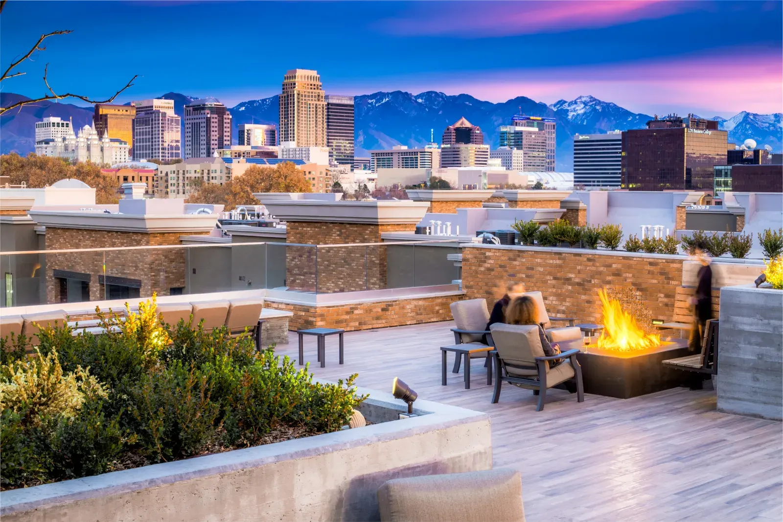 Residents beside a fire feature on the 4th West rooftop with the Salt Lake City skyline beyond
